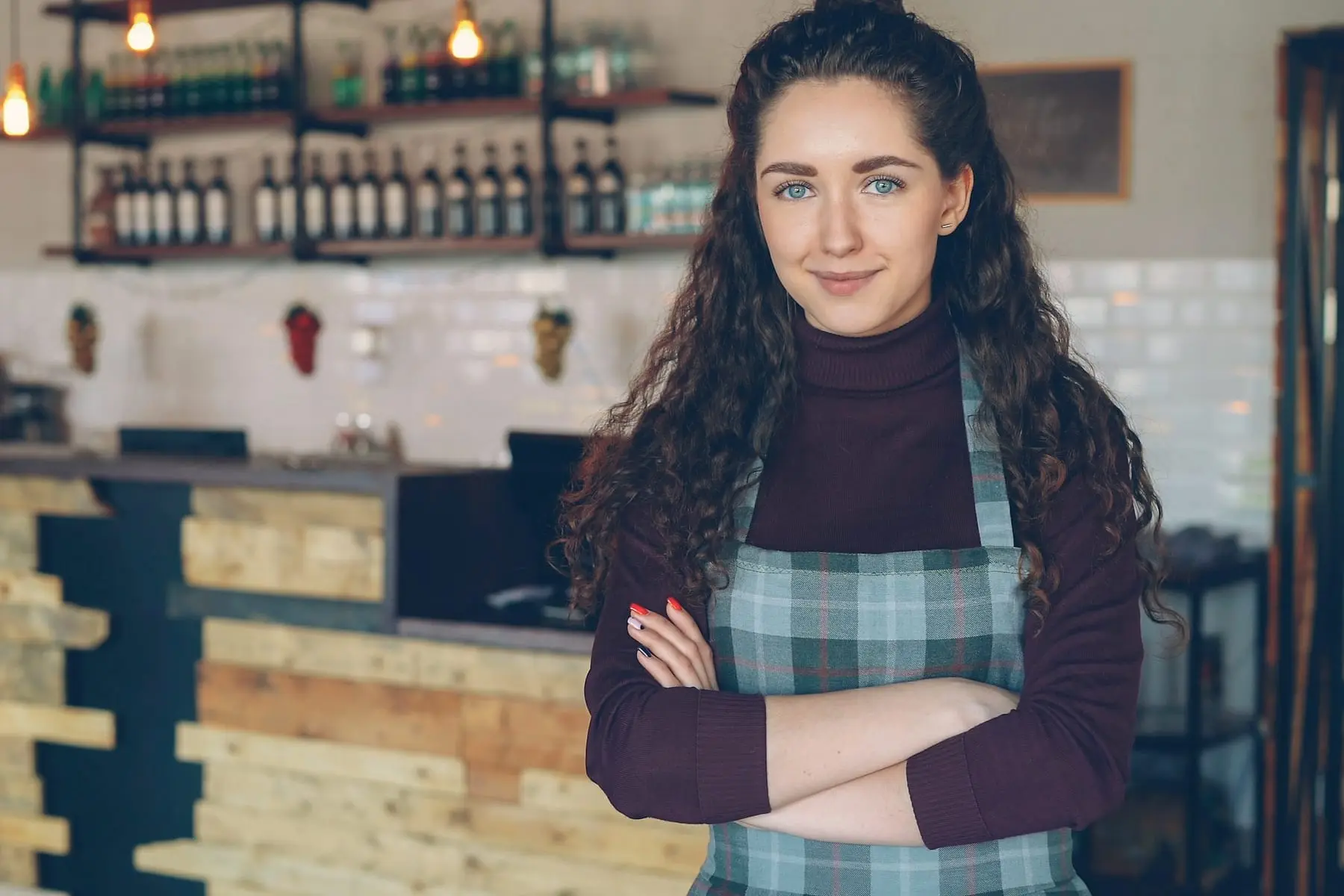 Commerçante en tablier, bras croisés, devant le comptoir en bois de sa boutique