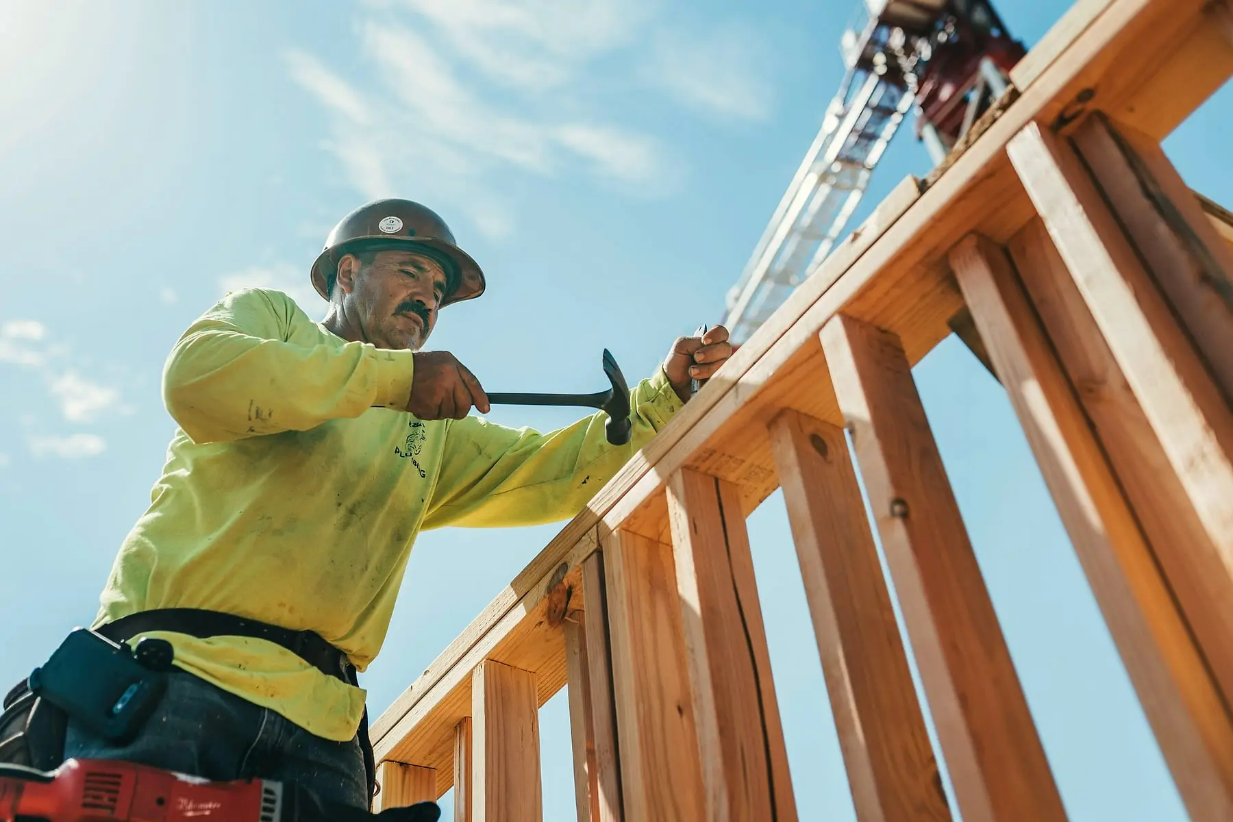 Charpentier casqué clouant une ossature en bois en plein soleil