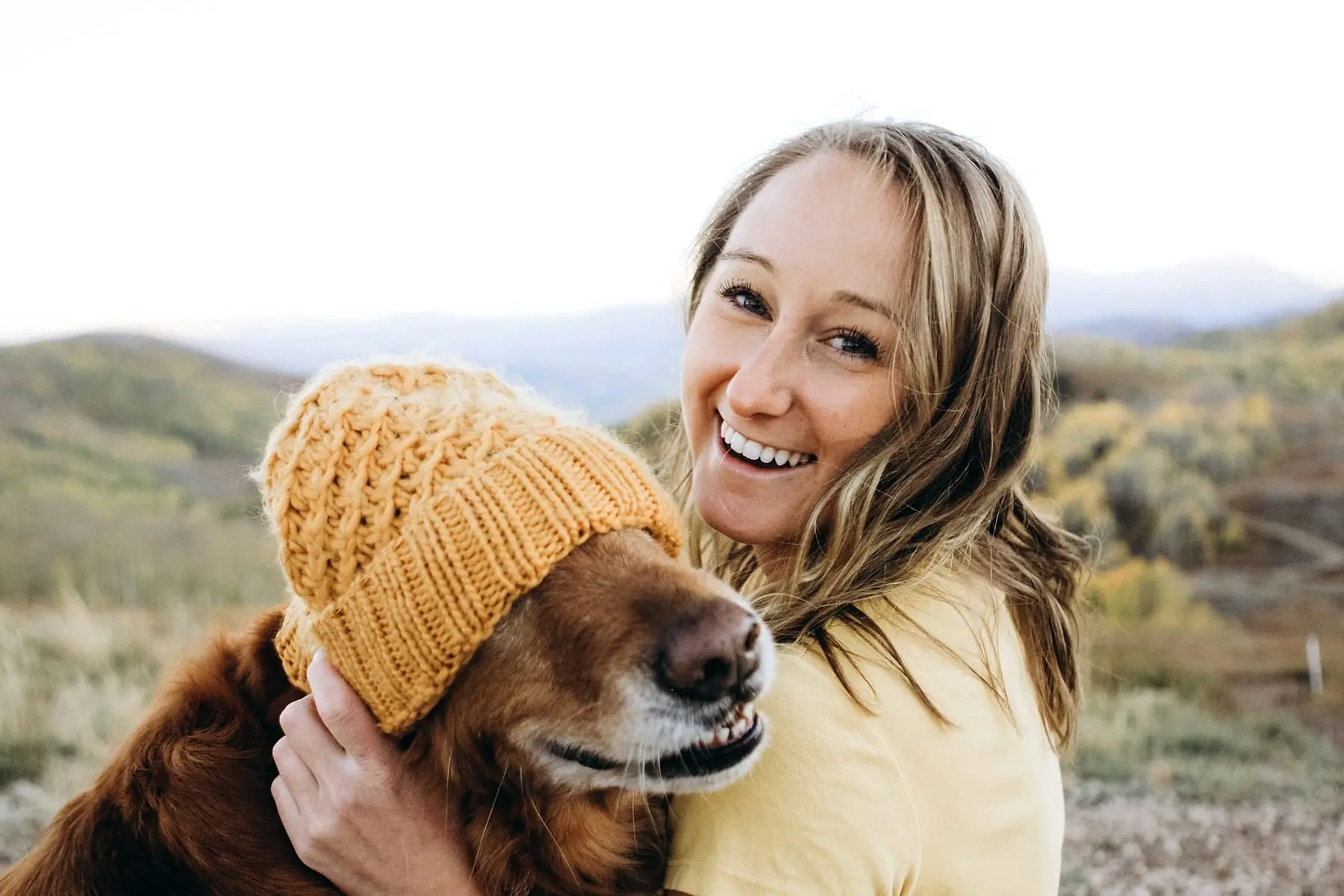 Jeune femme joue contre joue avec son chien coiffé d'un bonnet jaune