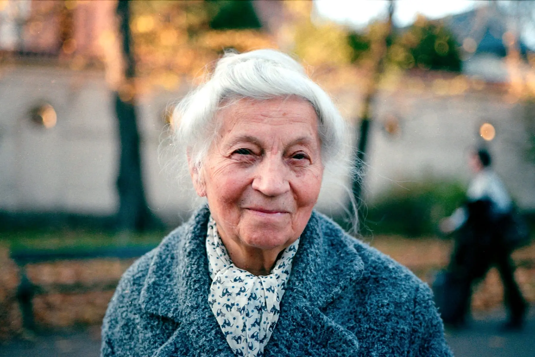 Dame âgée sereine dans une rue bordée d'arbres en automne