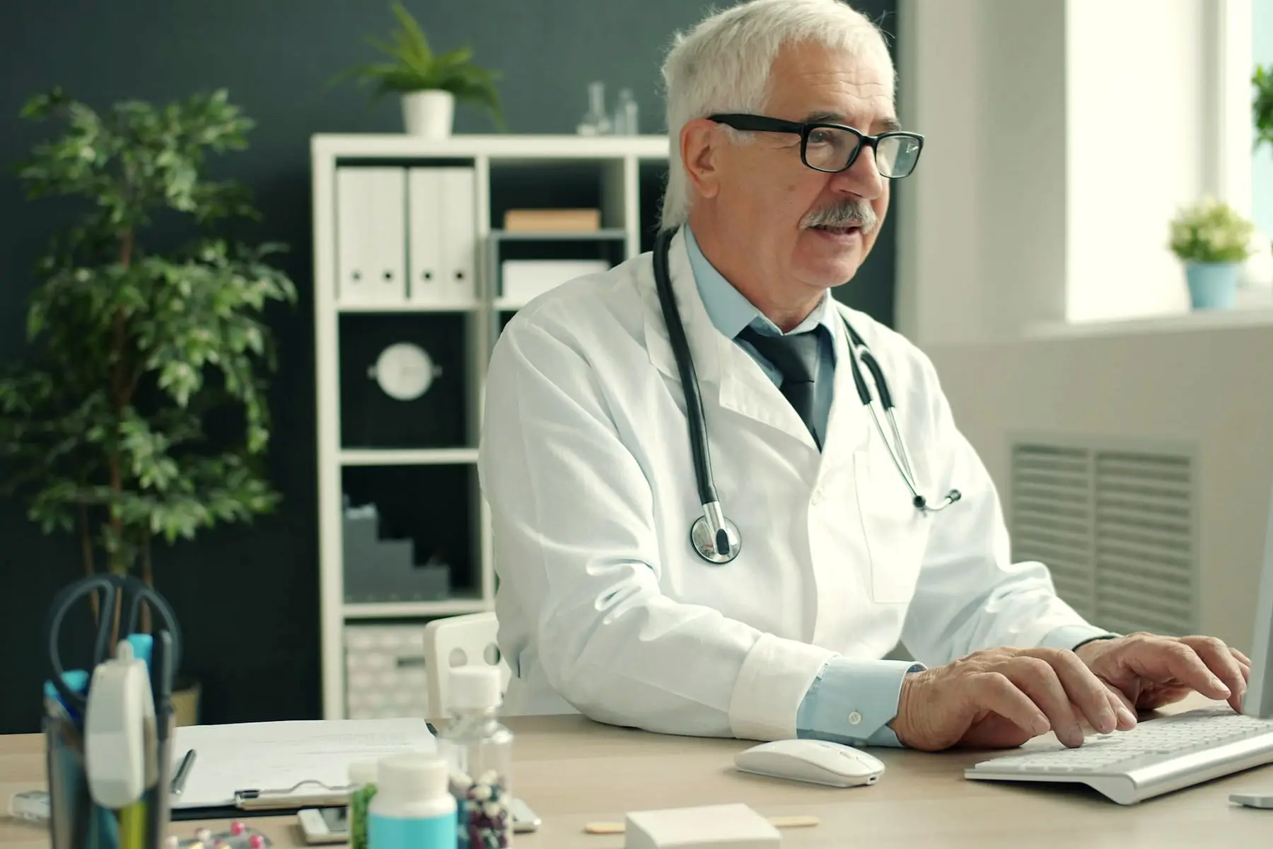 Médecin senior travaillant sur son ordinateur dans son cabinet