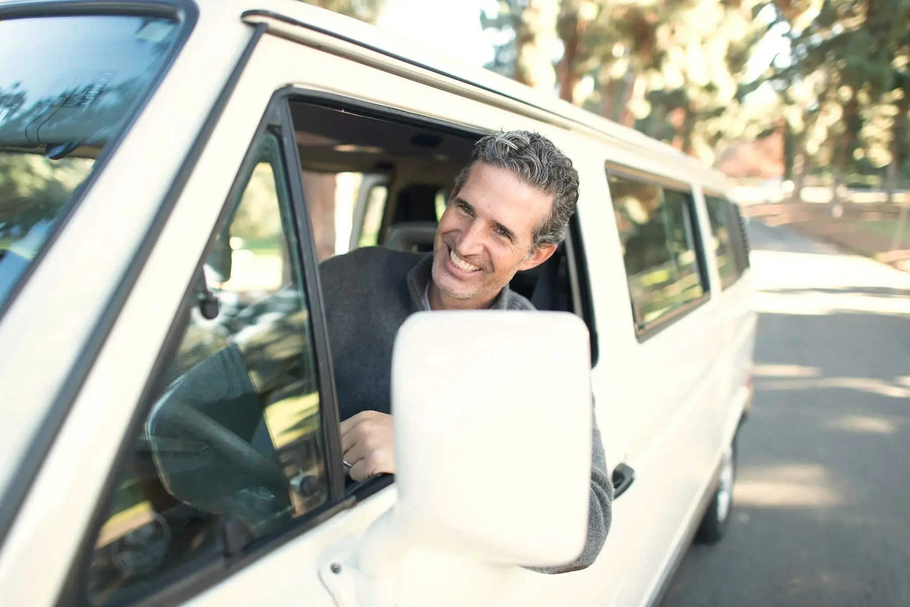 Chauffeur souriant à la fenêtre de son utilitaire blanc garé sous les arbres